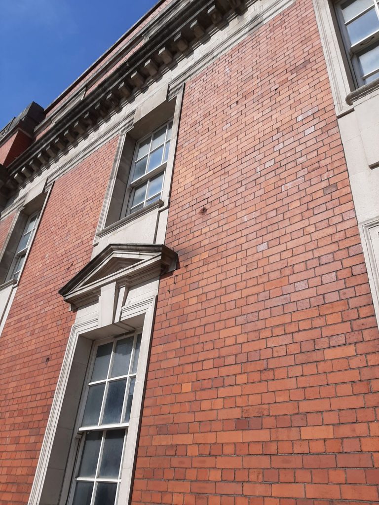 Llys Glas: Spot pockmarks in the red brick—shrapnel scars that still whisper stories of Swansea’s wartime resilience.